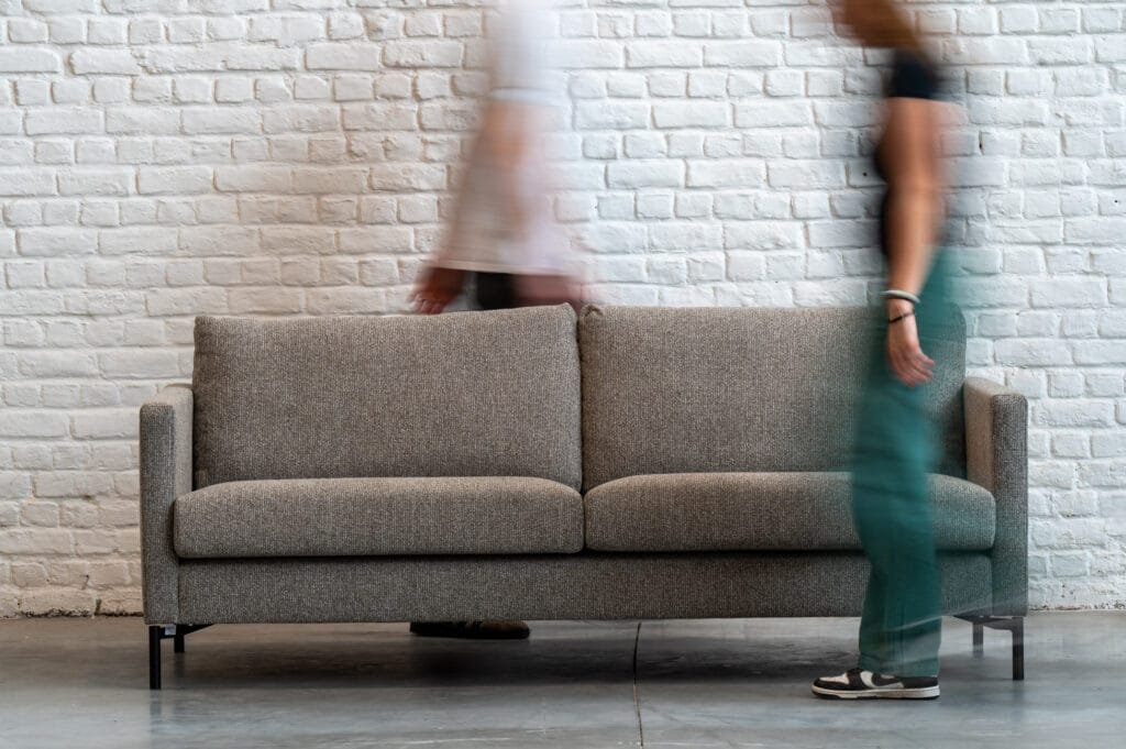 Deux personnes passent sournoisement devant un Canapé Impulse, tissu Sneak.