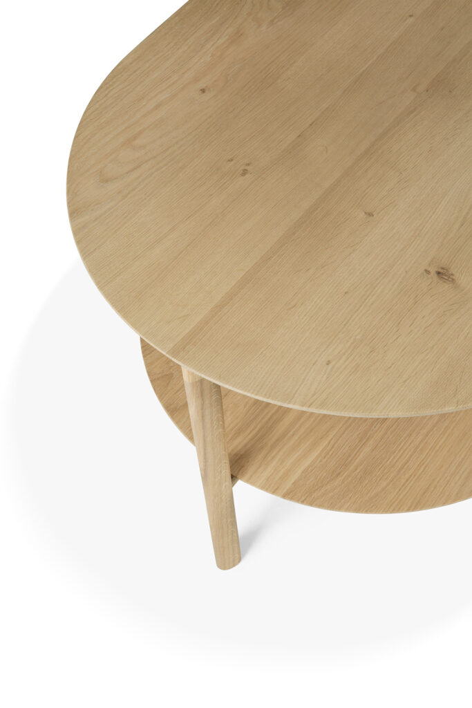 Une table basse ovale en bois avec une étagère inférieure, dotée d'une finition simple en grain de bois naturel et de trois pieds robustes, rappelant l'esthétique carrée de l'élégante table de salle à manger Bok.