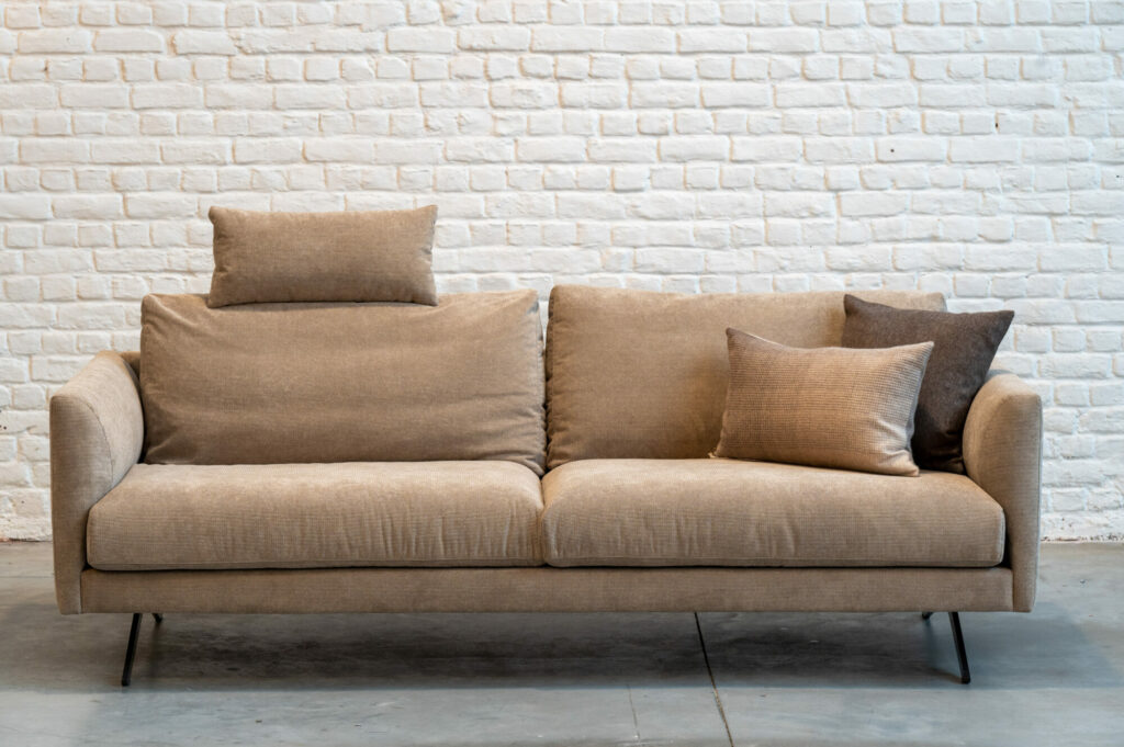Une Expo - Canapé Diva beige devant un mur de briques blanches.