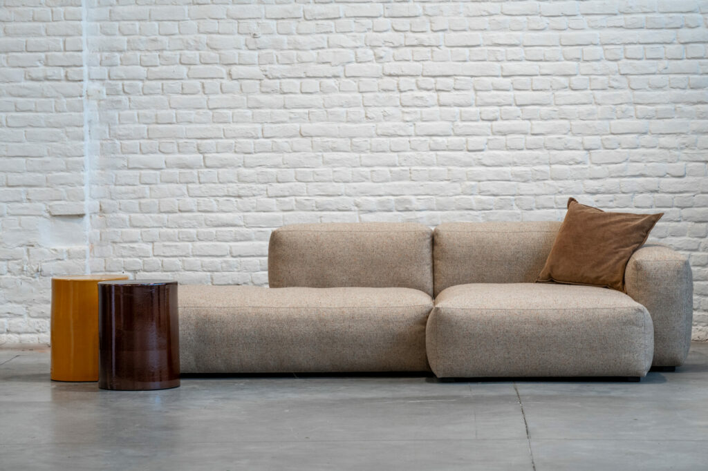 Un canapé beige Expo-Mags Soft S8265 Wide ChL low+S9301 Right Backrest-Bolgheri LGG devant un mur de briques.