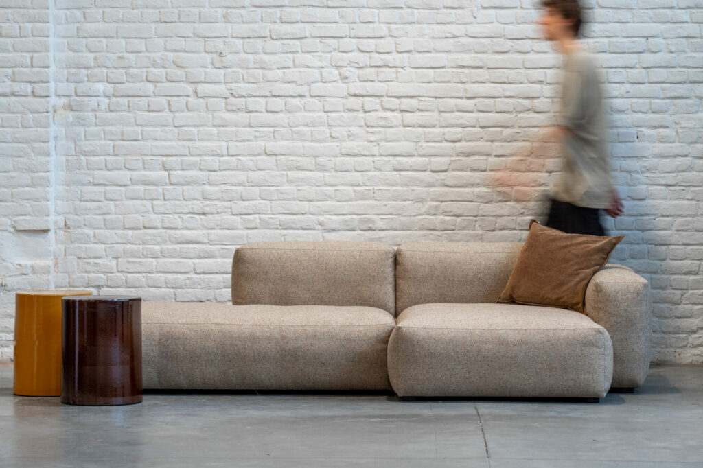Un homme passant devant un canapé avec un large Expo-Mags Soft S8265 Wide ChL low+S9301 Right Backrest-Bolgheri LGG dans un mur de briques.