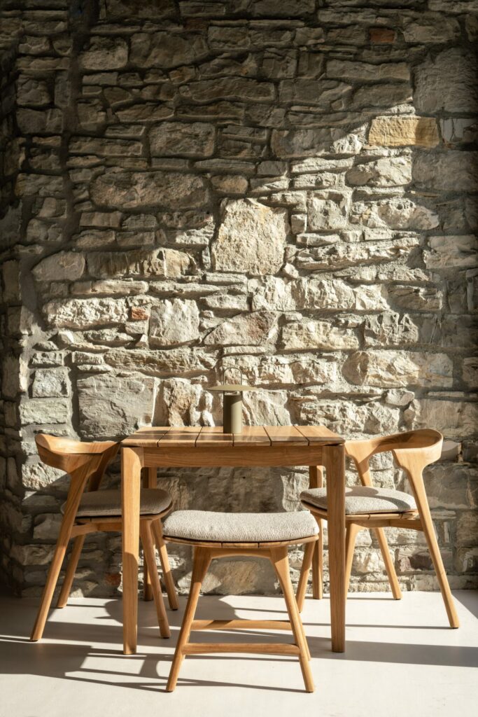 Une chaise de salle à manger d'extérieur Jack avec accoudoirs devant un mur de pierre.