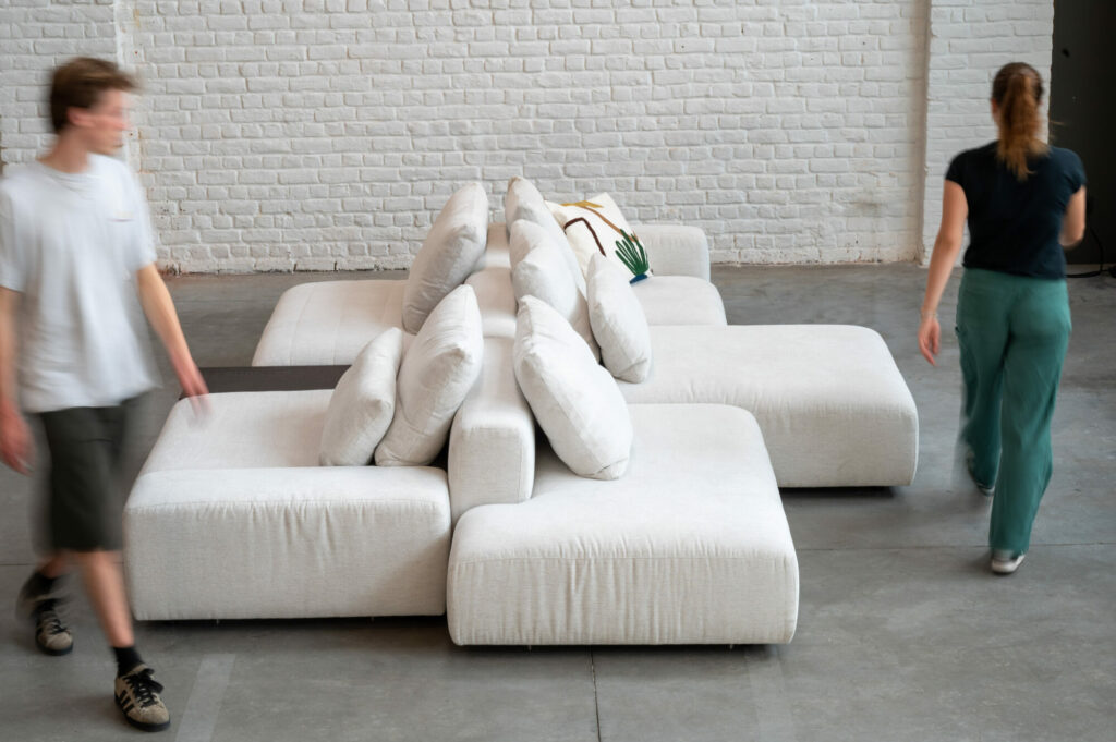 Deux personnes passant devant un Expo - Canapé Reverso blanc dans une pièce recouverte de tissu Cottage 3715 expo.