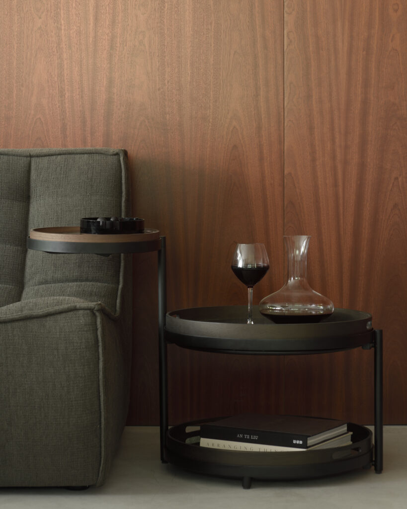 Un canapé gris avec un verre de vin sur une Table d'appoint à plateau pivotant.