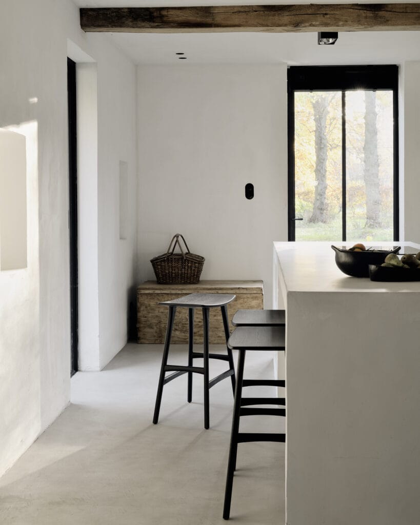 Une cuisine blanche avec poutres en bois et tabourets en chêne teinté noir.