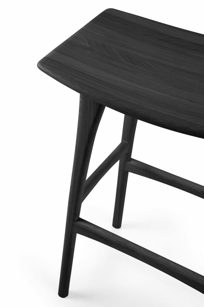 Un tabouret de bar en chêne teinté noir vernis posé sur un fond blanc.