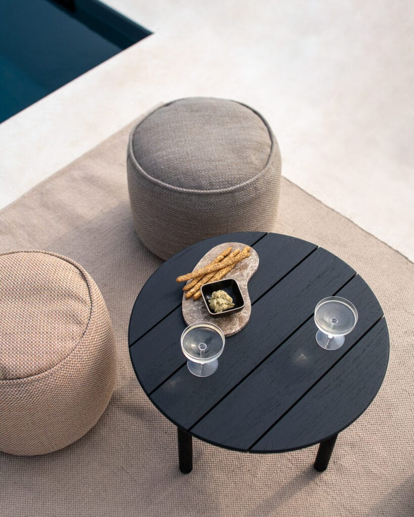 Une table basse de jardin Quatro avec une tasse de café et une bouteille de vin au bord d'une piscine.