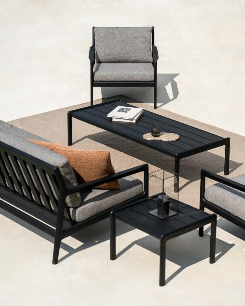 Un groupe de mobilier d'extérieur en teck, dont une table d'appoint teinté noir.