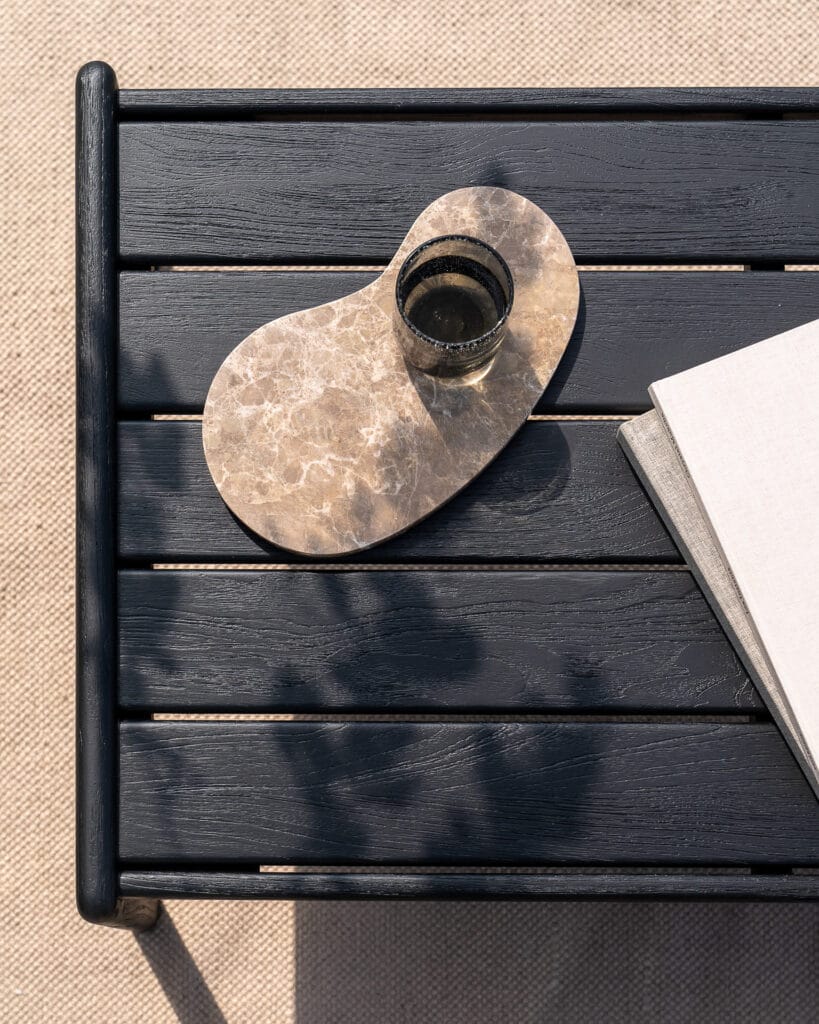 Une table d'appoint en teck noir avec un livre et une tasse de café.