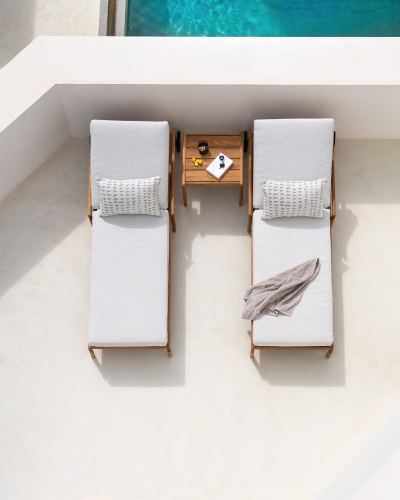 Deux chaises longues au bord d'une piscine avec des meubles en teck.