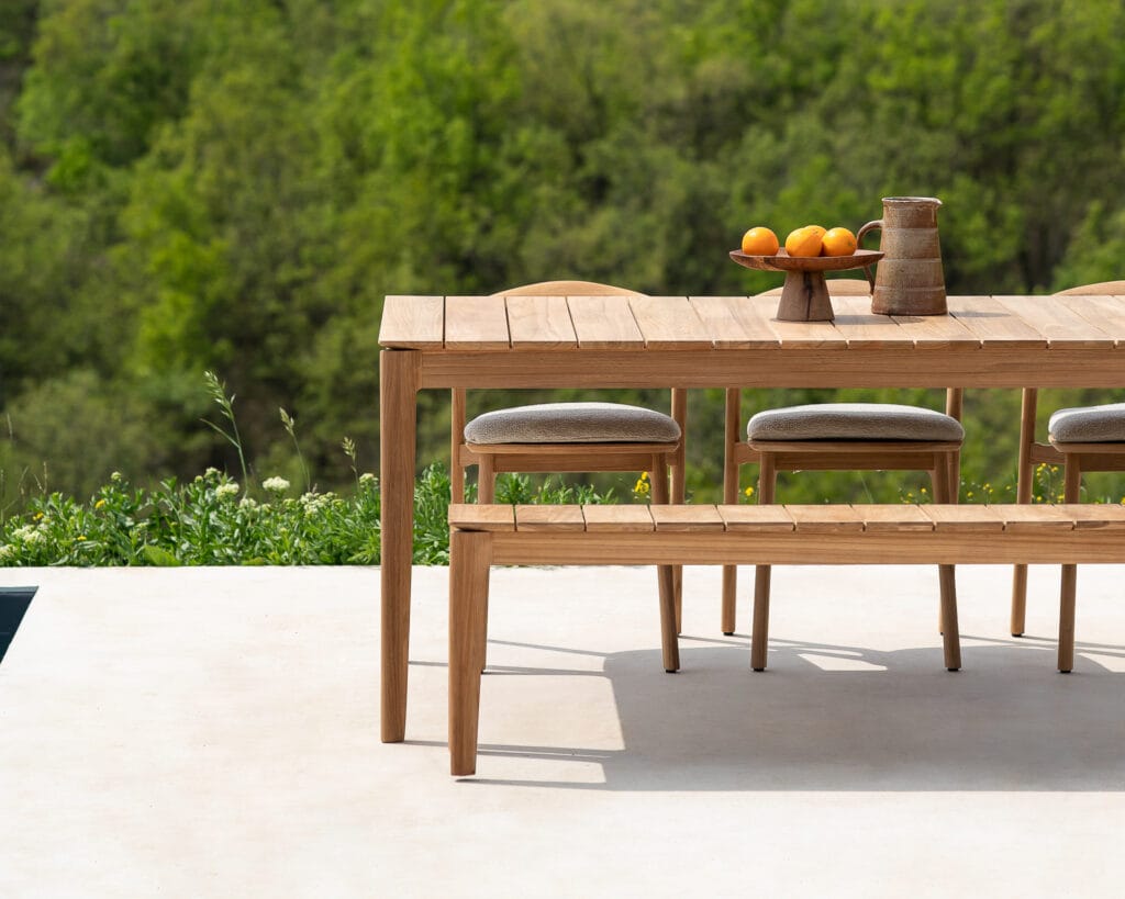 Un banc de jardin en teck naturel, accompagné d'une table en bois et de quatre chaises.