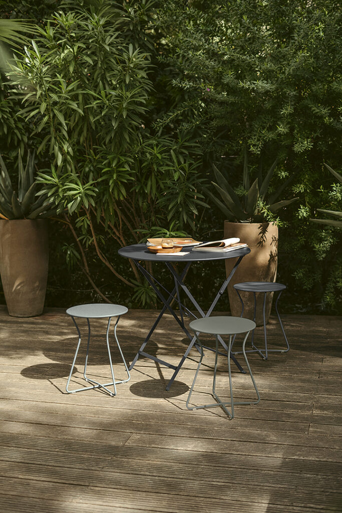 Une table et deux tabourets sur une terrasse en bois.