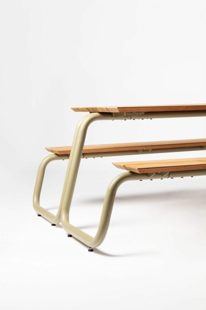 Vue latérale d'un banc moderne avec des lattes en bois et des pieds en métal gris clair sur fond blanc.