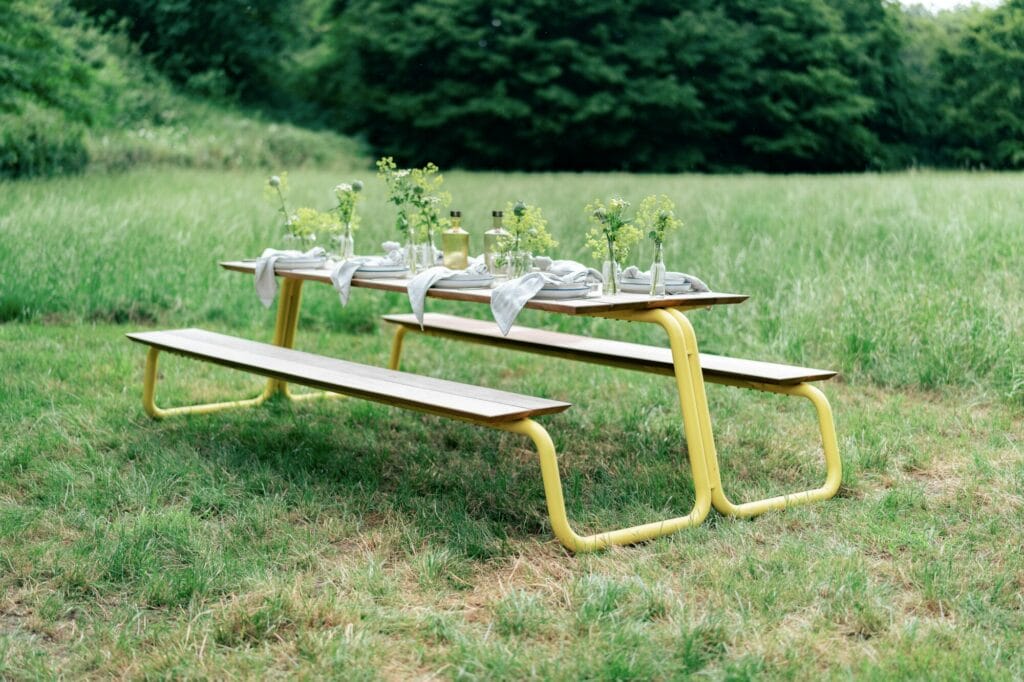 Une table de pique-nique extérieure, petite et peinte en gris clair RAL7044, installée pour un repas dans un champ herbeux.