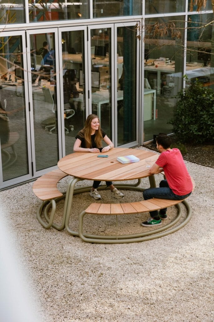 Deux personnes assises au Circle - set table + bancs - Gris clair (RAL7044) en plein air en train de discuter.