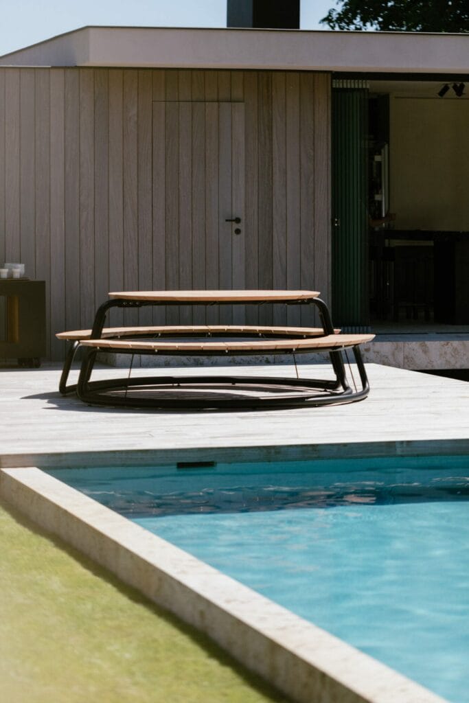 Mobilier d'extérieur moderne composé de The Circle - set table + bancs - Gris Clair (RAL7044) au bord d'une piscine, avec vue sur une maison contemporaine en arrière-plan.