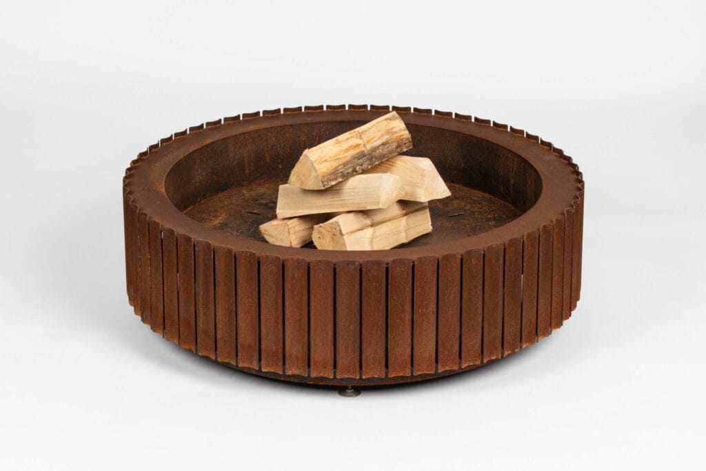 Foyer circulaire rustique en acier Corten avec bois de chauffage empilé à l'intérieur.
