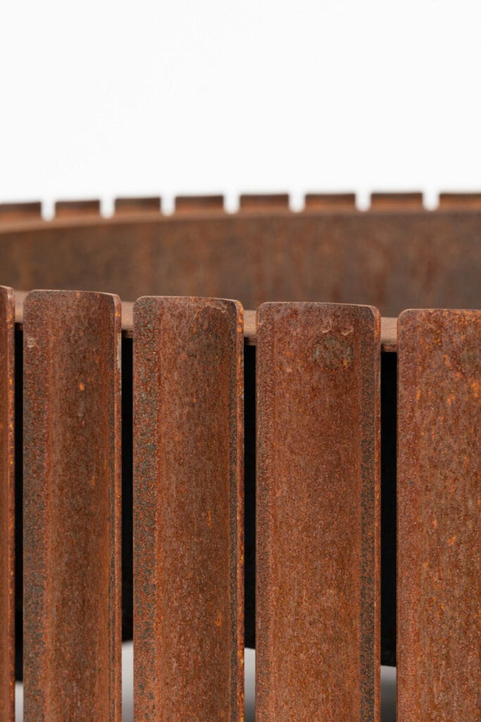 Gros plan d'une clôture en acier Corten rouillée avec des barres verticales sur fond blanc.