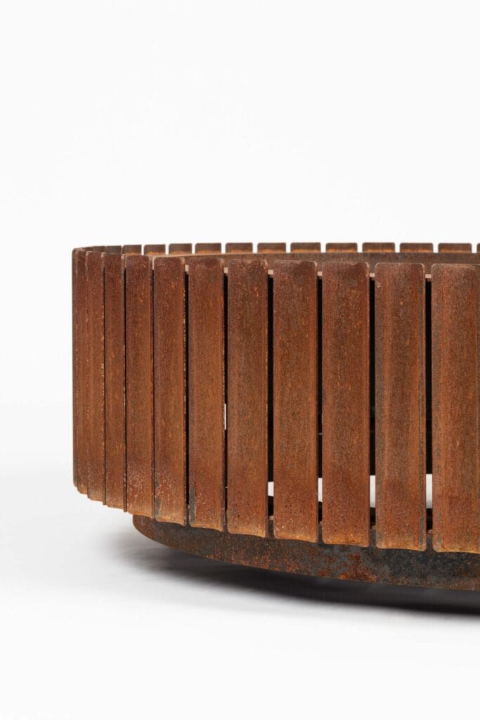 Objet circulaire rouillé en acier Corten avec lattes verticales sur fond blanc.