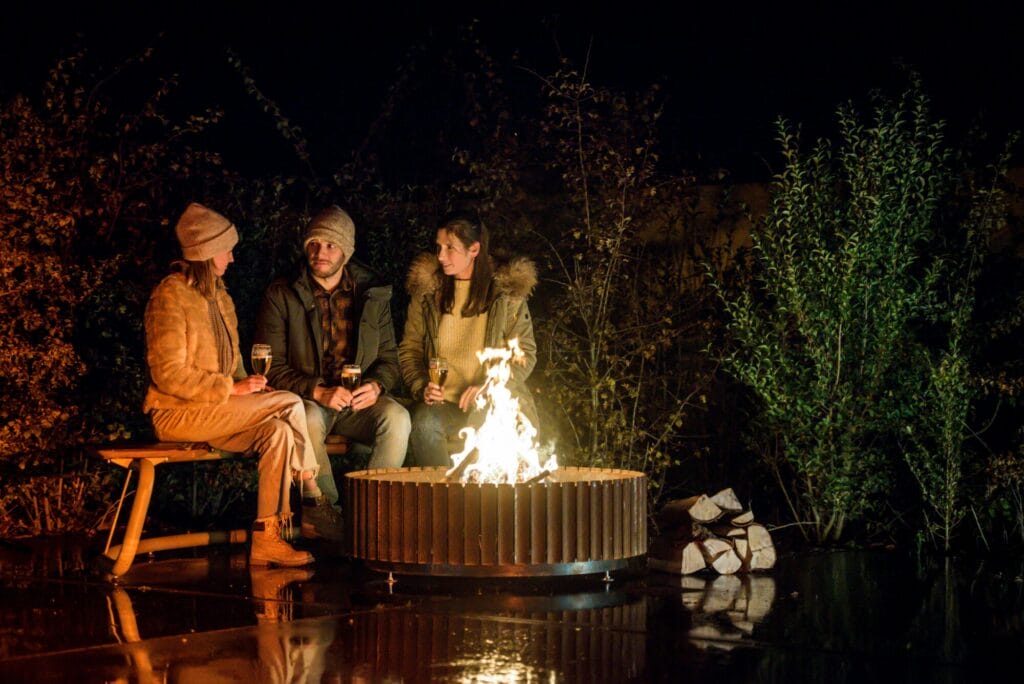 Trois personnes appréciant une conversation autour du foyer en acier Ring of Corten la nuit.