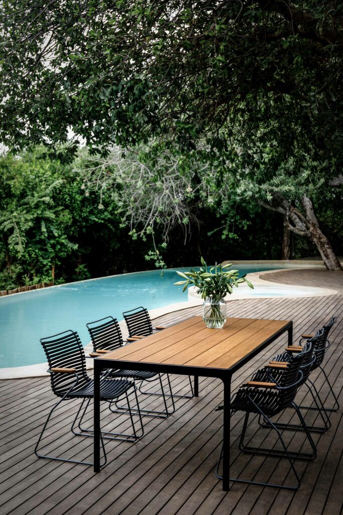Une table et une chaise Click avec accoudoirs au bord d'une piscine.