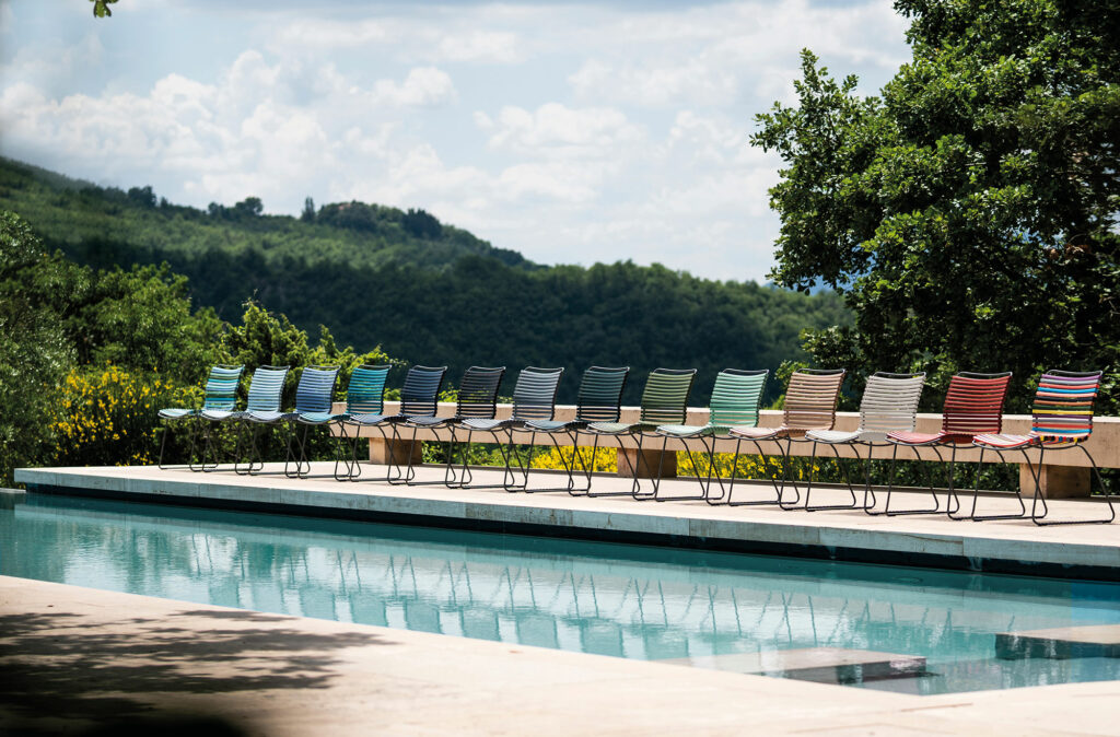 Une rangée de chaises longues colorées Chaise Click disposées au bord d’une piscine extérieure sereine, avec en toile de fond des collines verdoyantes.