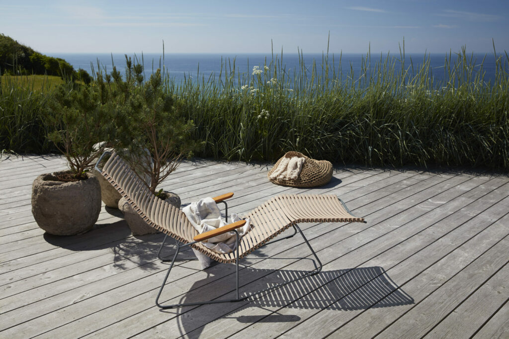 Coin détente face à la mer avec un Click Sunrocker, un plaid et un chapeau sur une terrasse en bois.