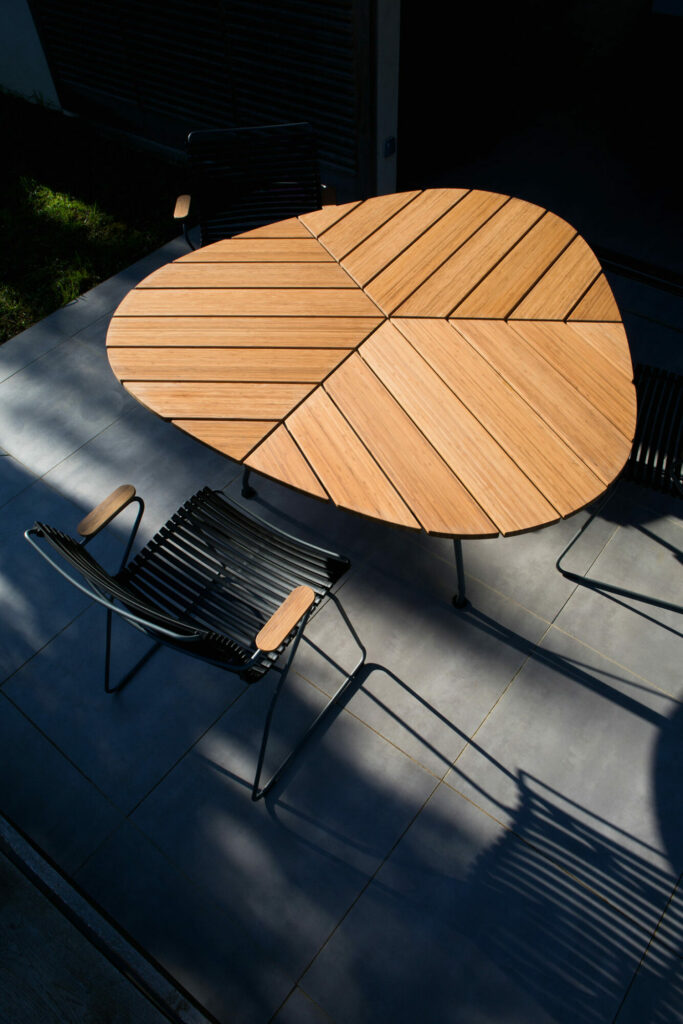 Table à manger d'extérieur moderne LEAF avec une table à manger ronde en bambou et des chaises noires, mises en valeur par un contraste de lumière du soleil et d'ombre.