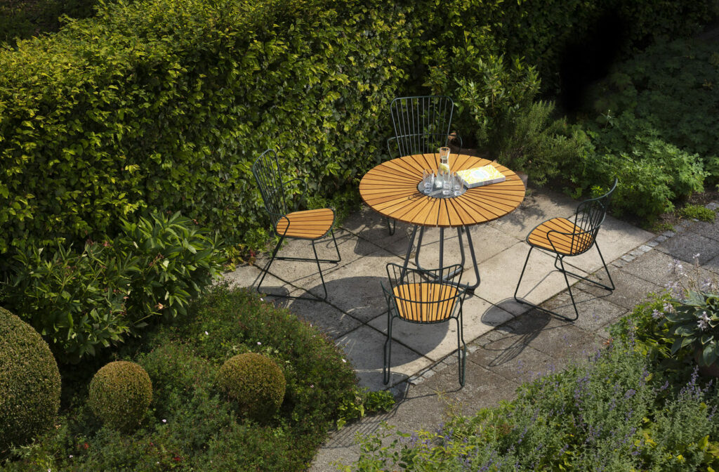 Aménagement de jardin patio avec une table à manger CIRCLE Ø110 avec un plateau en bambou et quatre chaises en métal entourées d'une verdure luxuriante.