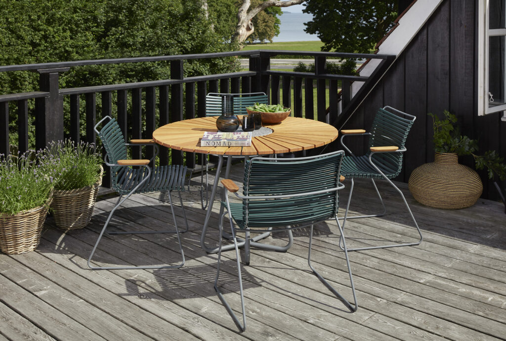 Ensemble de terrasse extérieure composé d'une table à manger CIRCLE, plateau Ø110 et chaises en métal sur une terrasse en bois entourée de verdure.