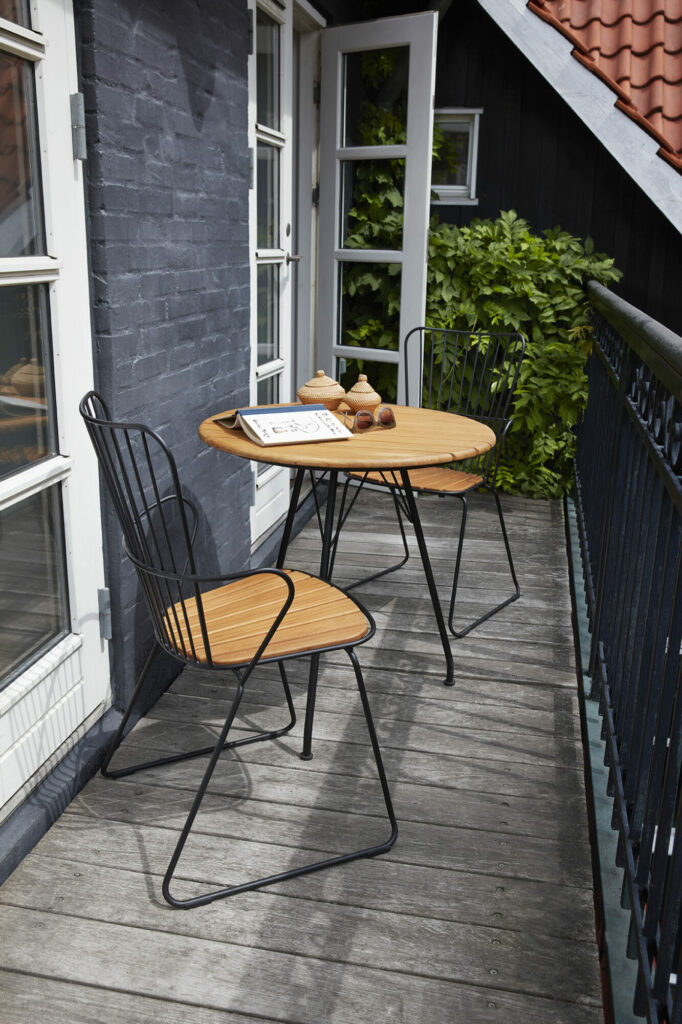 Un petit balcon avec une table bistrot, deux chaises PAON Dining dont une assise en bambou et un livre ouvert, suggérant un endroit cosy pour se détendre.