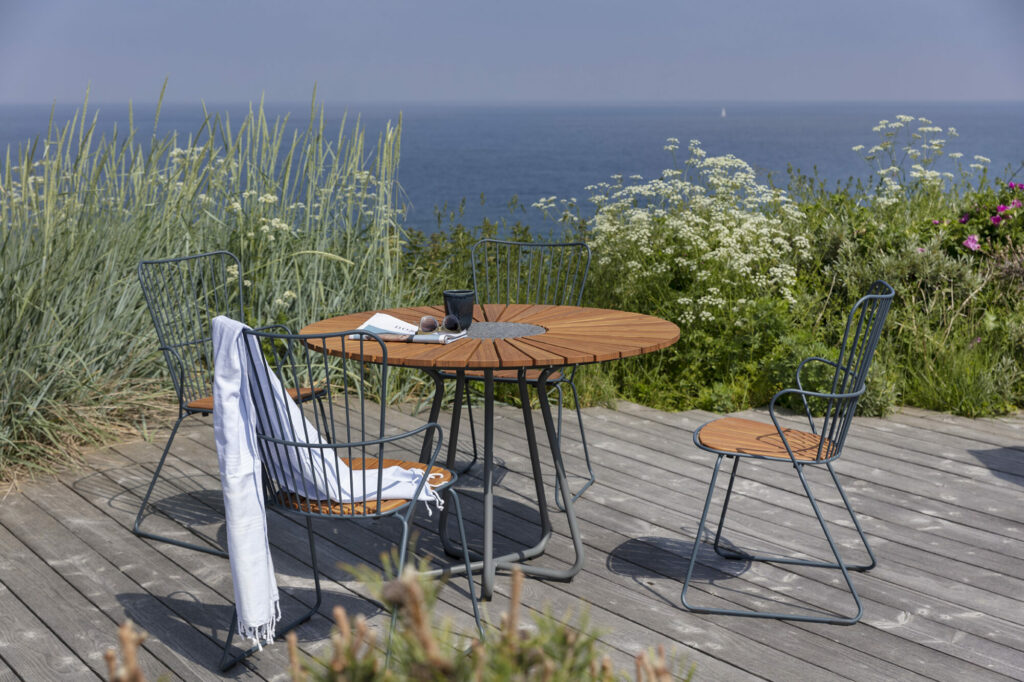 Coin salon extérieur avec un siège en bambou blanc, deux chaises PAON Dining et une vue sur l'océan.