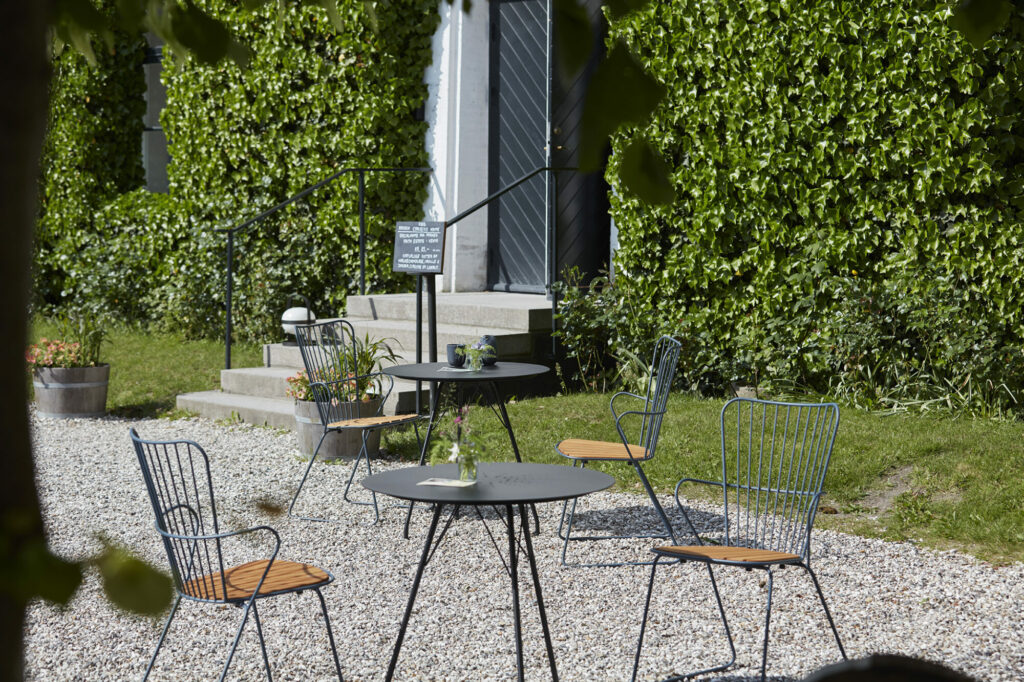 Un coin salon extérieur tranquille avec des chaises et des tables de salle à manger PAON en bambou blanc sur fond d'un mur de lierre vert luxuriant.
