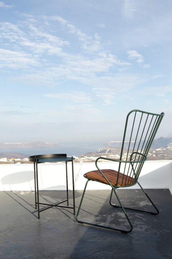 Une chaise longue Paon moderne et une petite table sur un balcon donnant sur un paysage côtier.