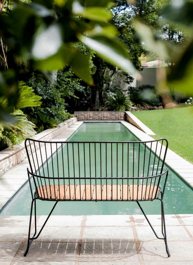 Un banc PAON en bambou blanc donnant sur une étroite piscine rectangulaire entourée d'une verdure luxuriante.