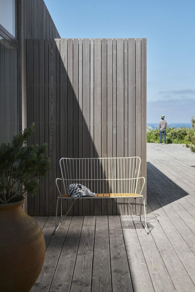 Coin salon extérieur moderne avec un banc PAON en bambou blanc, une terrasse en bois et une personne bénéficiant d'une vue lointaine.