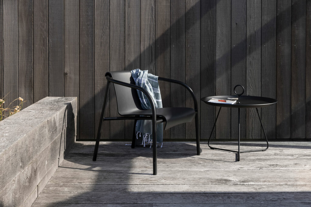 Configuration de mobilier d'extérieur moderne avec une chaise noire élégante et une table plateau EYELET noire Ø45 sur un fond en bois dans un cadre ensoleillé.
