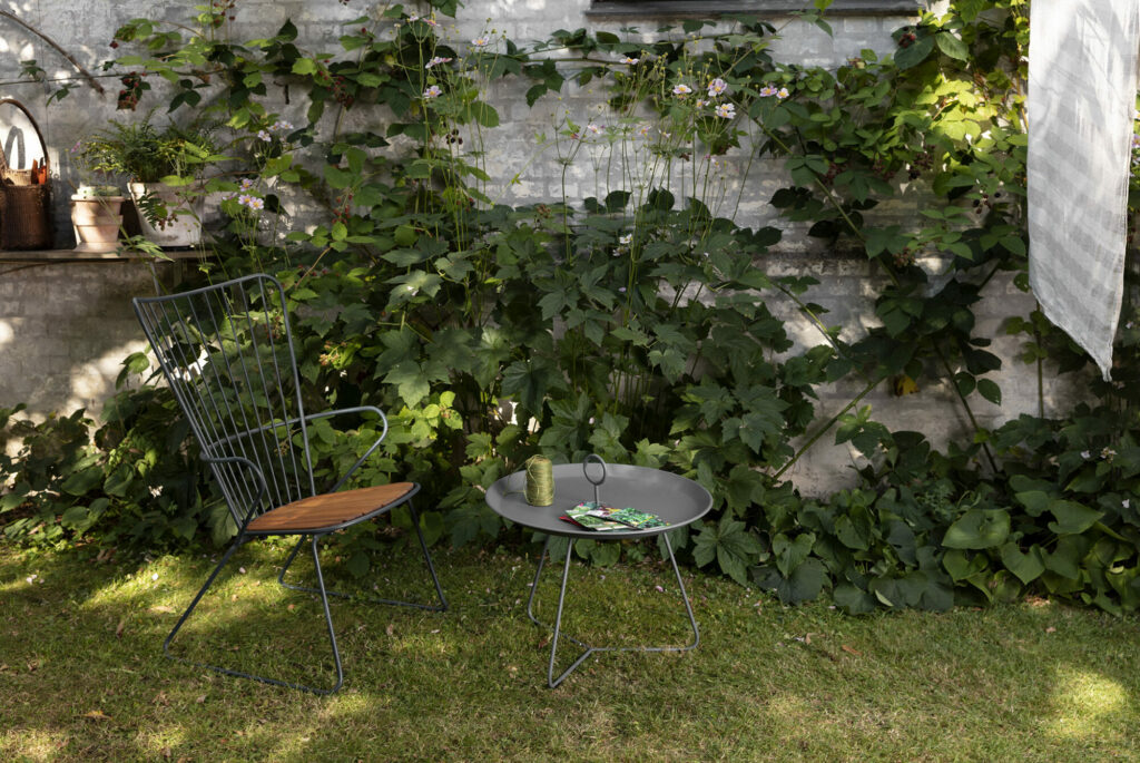 Un coin de jardin tranquille avec une chaise en métal et une table EYELET Tray Ø45, Noir entourée d'une verdure luxuriante.