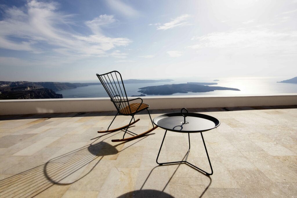Une chaise et une table plateau EYELET Ø45 de couleur noire sur un balcon offrant une vue panoramique sur la mer et le littoral.