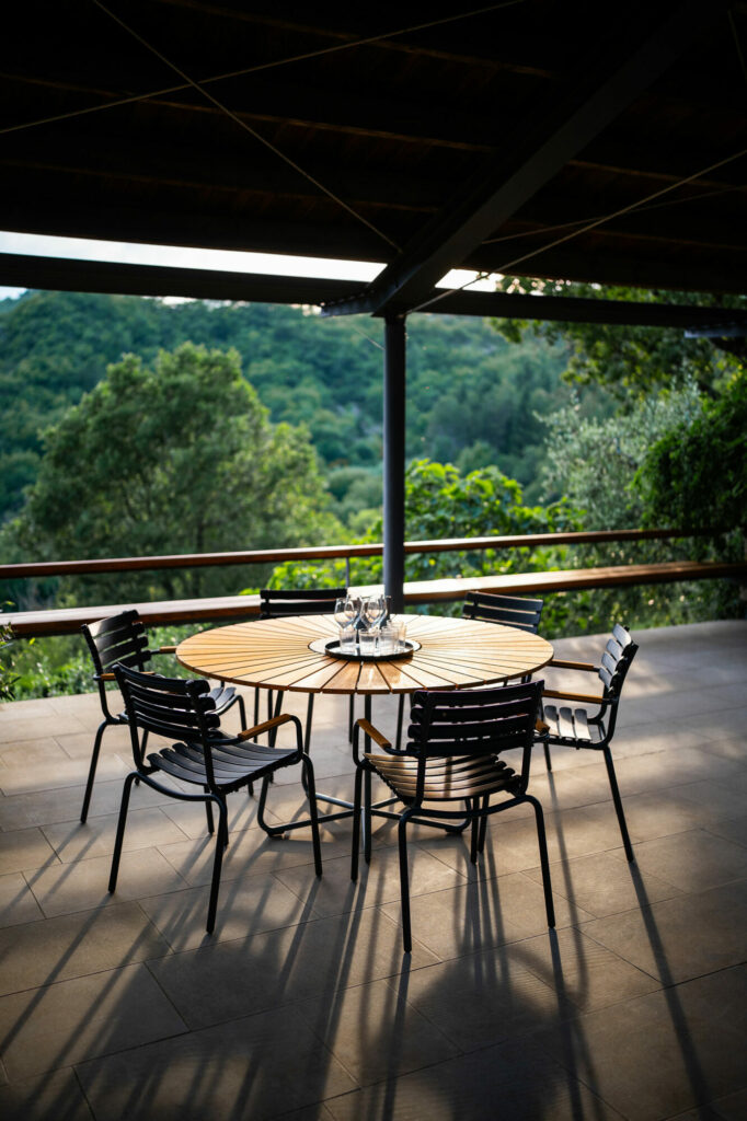 Configuration de salle à manger extérieure avec une chaise de salle à manger ReCLIPS bleu ciel dotée d'un accoudoir en bambou, autour d'une table ronde sur une terrasse donnant sur un paysage verdoyant.