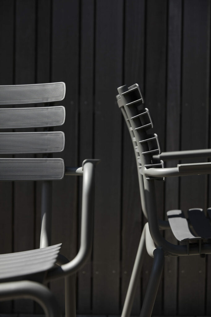 Chaise de salle à manger ReCLIPS de couleur bleu ciel avec accoudoir en bambou projetant des ombres sur un fond en bois.