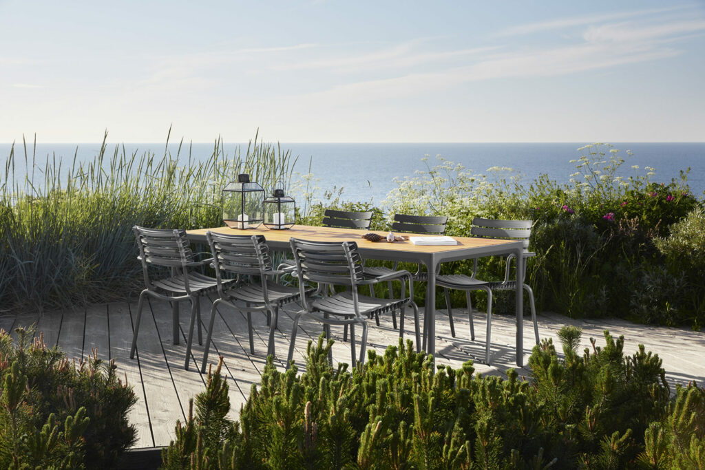 Configuration de salle à manger extérieure avec une table en métal et une chaise de salle à manger ReCLIPS bleu ciel avec accoudoirs en bambou sur une terrasse en bois surplombant la mer.