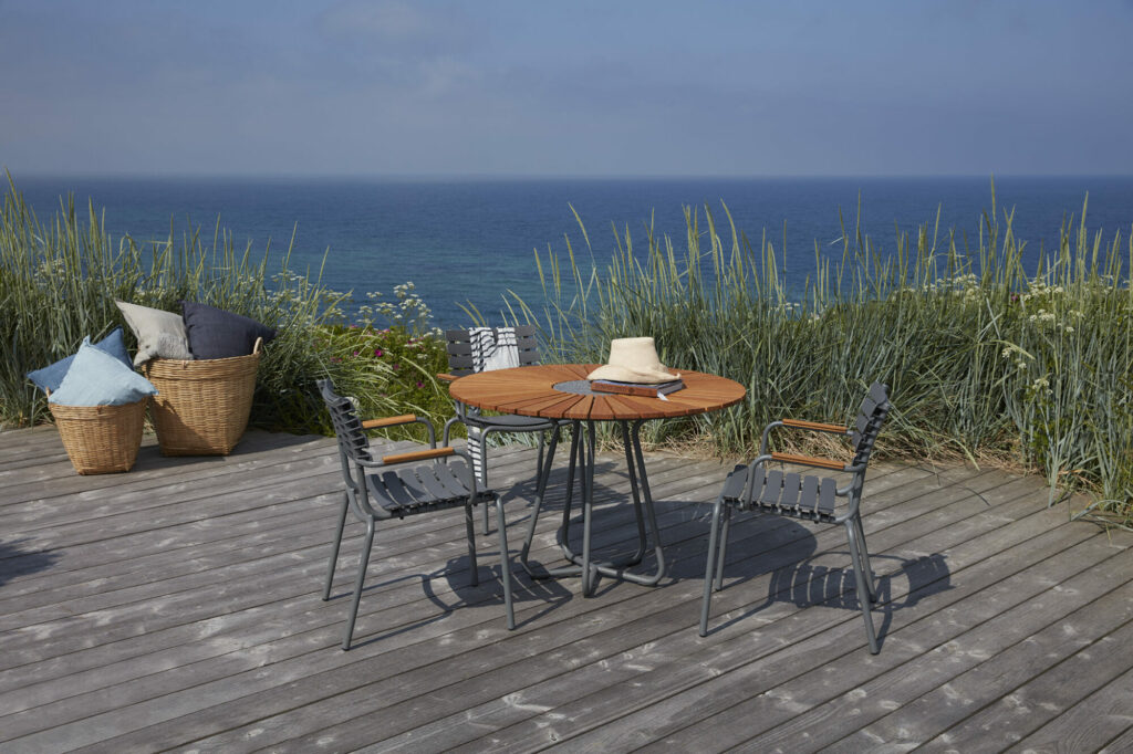 Disposition des sièges extérieurs avec vue sur la mer avec une chaise de salle à manger ReCLIPS bleu ciel dotée d'un accoudoir en bambou et d'un chapeau de paille sur la table.
