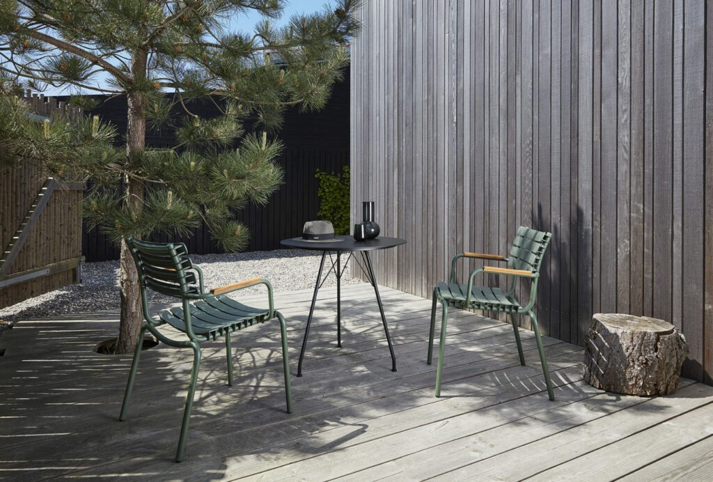 Terrasse extérieure avec deux chaises ReCLIPS Dining en bleu ciel, une table ronde et une souche de bois contre un mur à lattes de bois.