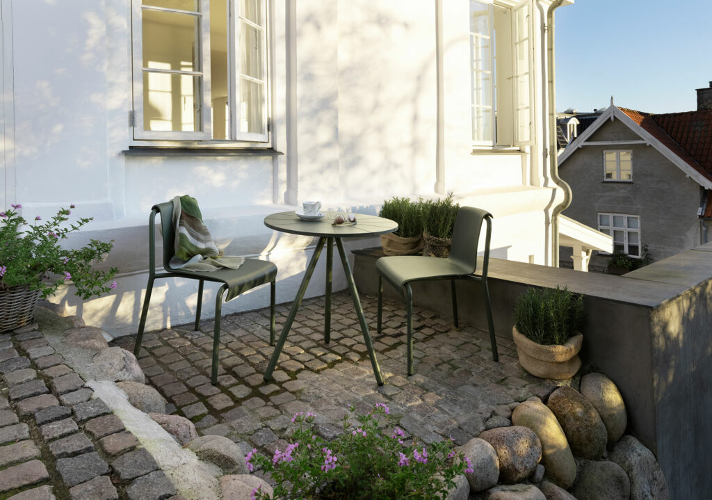 Patio sur le toit avec deux chaises noires NAMI Dining et une table dressée pour le petit-déjeuner, donnant sur les bâtiments historiques.