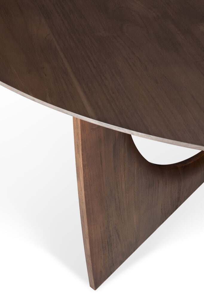 Gros plan d'une table en teck verni avec un plateau rond et un design unique de pieds incurvés. La finition sombre accentue le grain naturel, faisant de cette table à manger géométrique - teck verni - marron - une superbe pièce maîtresse.