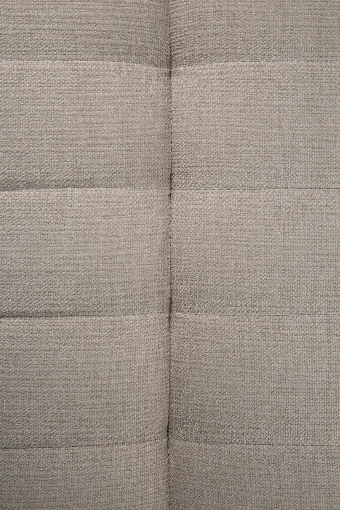 Gros plan d'un tissu gris texturé et rembourré avec des lignes de couture horizontales, rappelant le savoir-faire raffiné du Canapé N701.
