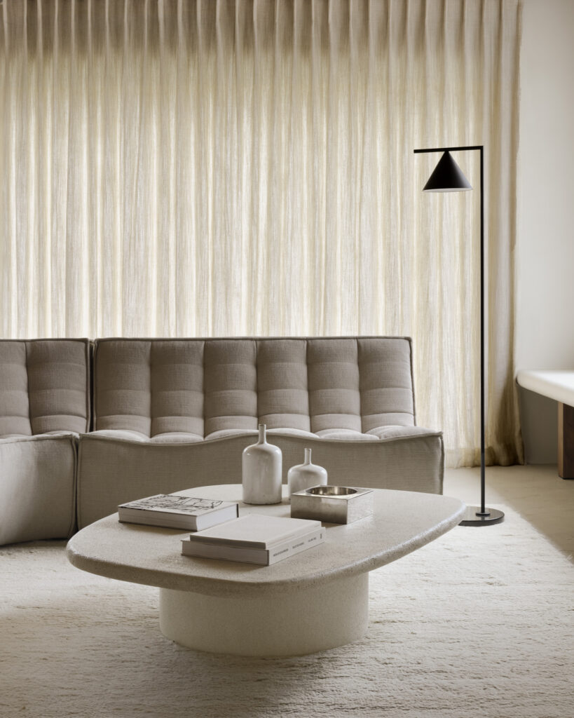 Un salon moderne comprend un Canapé N701 gris, un canapé 2 places en tissu écologique écru, une table basse blanche avec des objets de décoration, un lampadaire noir et des rideaux de couleur claire.