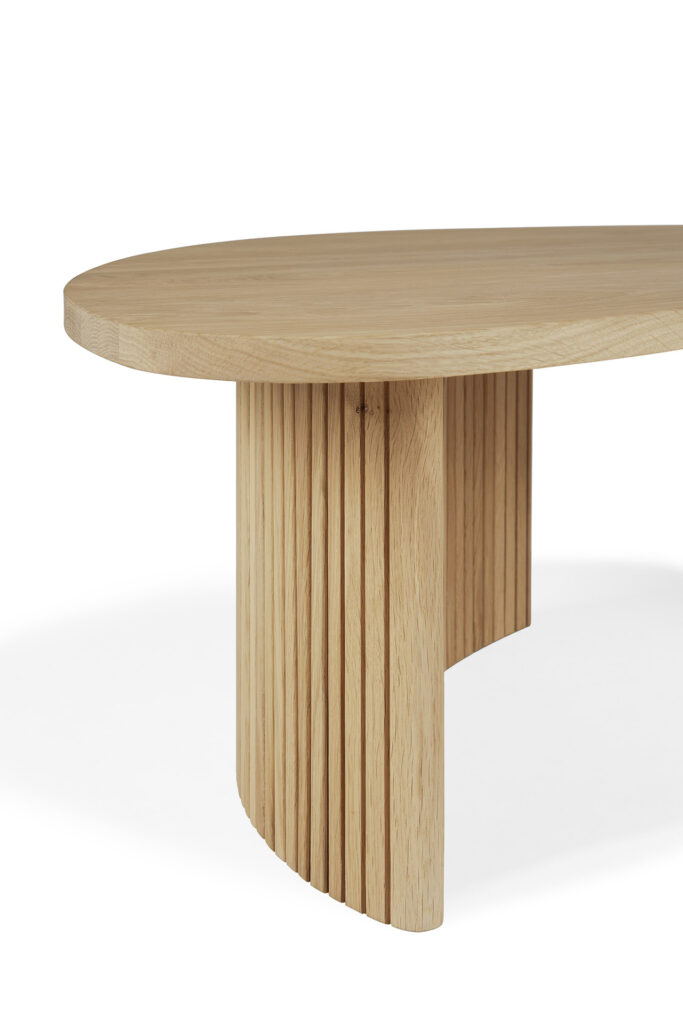 Une table en bois avec un plateau ovale et lisse en chêne naturel, doté d'une base au design unique avec des lattes verticales.