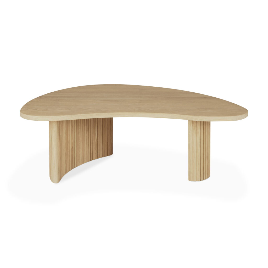 Une table basse en bois avec un plateau en forme de boomerang et un piètement constitué de lattes verticales. La table est finie dans un ton chêne naturel clair.